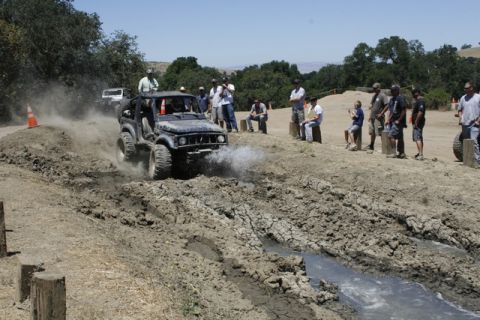 1989 Ford Bronco - An off-road vehicle navigates a muddy track while onlookers observe the event.