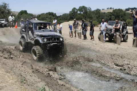 1989 Ford Bronco - An off-road vehicle navigates a muddy track, kicking up water and dirt.