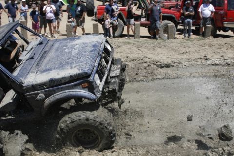 1989 Ford Bronco - A blue off-road vehicle navigates a muddy obstacle course with spectators watching in the background.