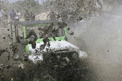 1989 Ford Bronco - An off-road vehicle navigates a muddy course, kicking up a large spray.