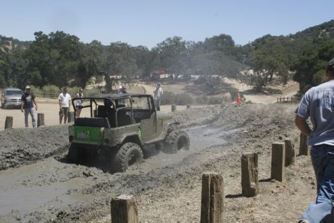 1989 Ford Bronco - A green off-road jeep struggles through a muddy track during an event, with onlookers observing the challenging terrain.