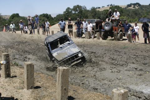 1989 Ford Bronco - An off-road vehicle struggles in a mud pit during an event with onlookers.