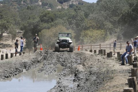 1989 Ford Bronco - A Toyota Land Cruiser FJ40 tackles a challenging mud obstacle with onlookers observing the event.