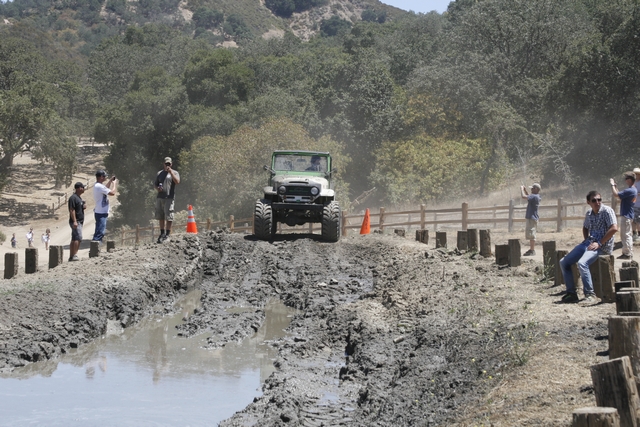 Green Toyota Land Cruiser FJ40 driving through mud, spectators watching
