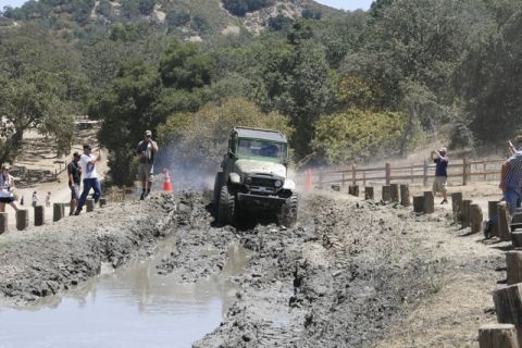 1989 Ford Bronco - An off-road vehicle navigates a challenging muddy course on a sunny day.