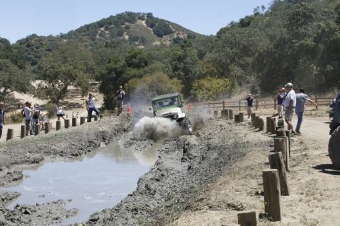 1989 Ford Bronco - An off-road vehicle navigates a muddy course during an event, with onlookers observing from the side.