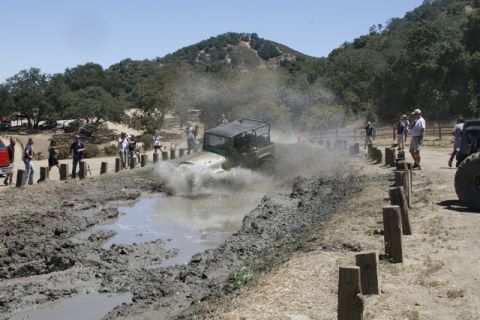 1989 Ford Bronco - Spectators watch as a green off-road vehicle navigates a muddy obstacle course, kicking up a large spray.