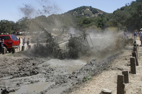 1989 Ford Bronco - An off-road vehicle creates a large splash as it navigates a muddy course, with a red SUV observing.