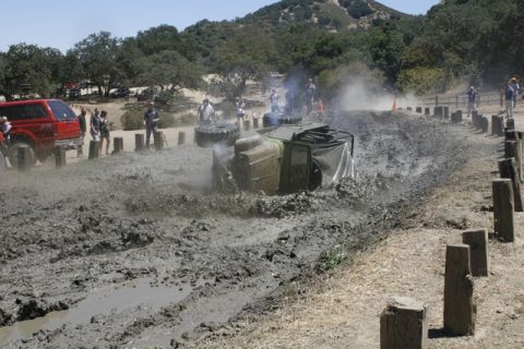 1989 Ford Bronco - A vehicle is stuck and overturned in a muddy obstacle course while onlookers observe.