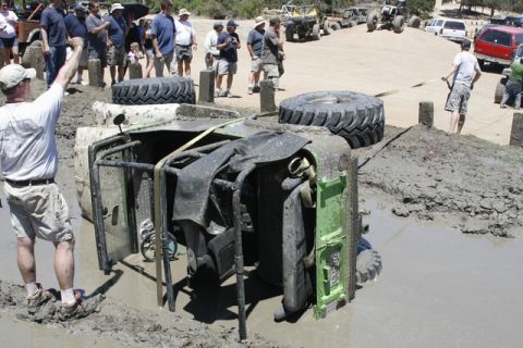 1989 Ford Bronco - An overturned off-road vehicle is stuck in thick mud, with onlookers and other vehicles in the background.