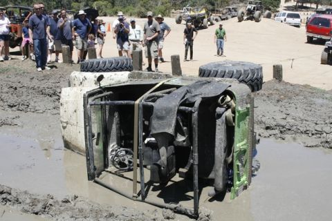 1989 Ford Bronco - An off-road vehicle has overturned in a mud pit, with a crowd of onlookers observing the scene.