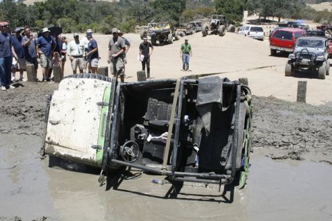 1989 Ford Bronco - An off-road vehicle has overturned in a mud pit, with onlookers observing the scene.