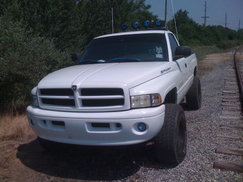 2001 Dodge 1500 - This white Dodge pickup truck is parked next to a set of railroad tracks, with off-road lights mounted on its roof.