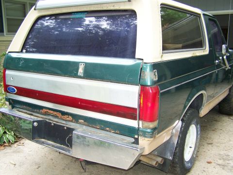 1989 Ford Bronco - The rear of a two-tone green and tan Ford Bronco shows some rust on the bumper and a two-tone stripe detail.