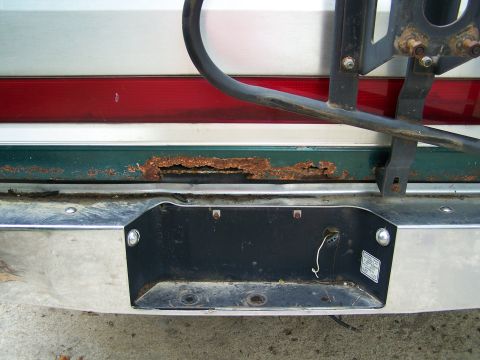 1989 Ford Bronco - The rear bumper and license plate area of a vehicle are visible, with significant rust on the body panel.