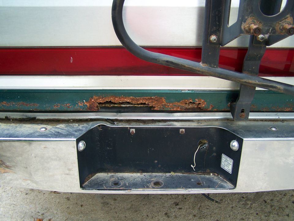 Rear bumper with license plate area, showing rust on the green body panel above