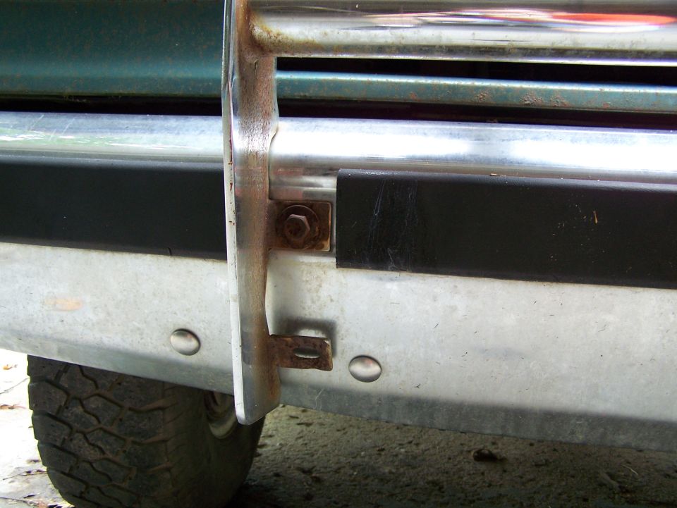 close-up of a vehicle's front bumper and brush guard, showing some rust on the mounting hardware
