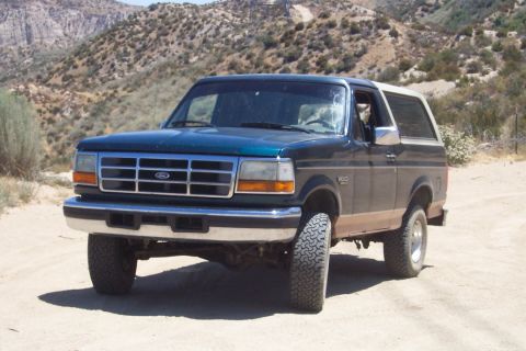 1995 Ford Bronco - A Ford Bronco is parked on a dusty road with arid hills behind it.