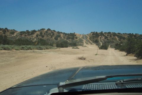 1995 Ford Bronco - View from inside a vehicle looking out at a desert landscape with a dirt road winding through hills.
