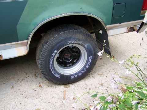 1989 Ford Bronco - Close-up of a truck's rear wheel and fender, showing some rust and a mud flap.
