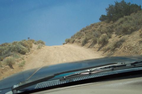 1995 Ford Bronco - View from inside a vehicle driving on a dusty, uphill dirt road with sparse vegetation under a clear blue sky.