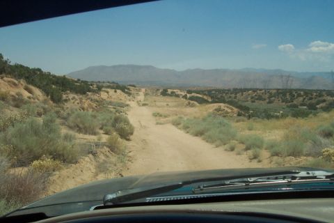 1995 Ford Bronco - The view from inside a vehicle shows a dirt road leading through a dry, scrub-covered desert landscape towards distant mountains.