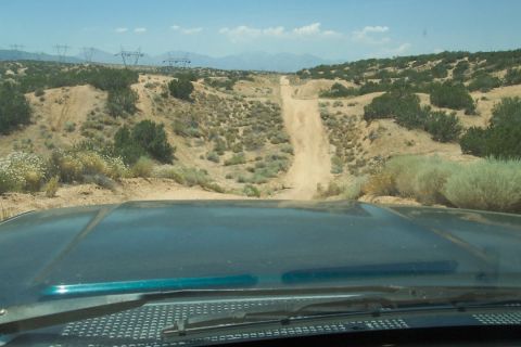 1995 Ford Bronco - Driving up a steep, dusty trail in a desert environment with mountains and power lines visible.