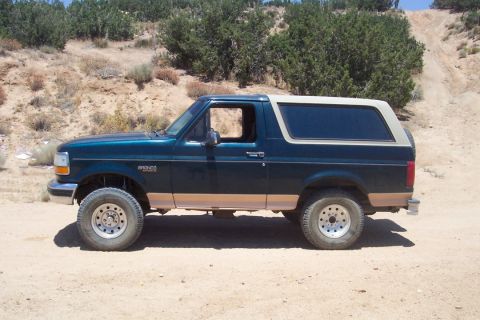 1995 Ford Bronco - Side view of a green 1995 Ford Bronco with tan trim parked on a dirt road.