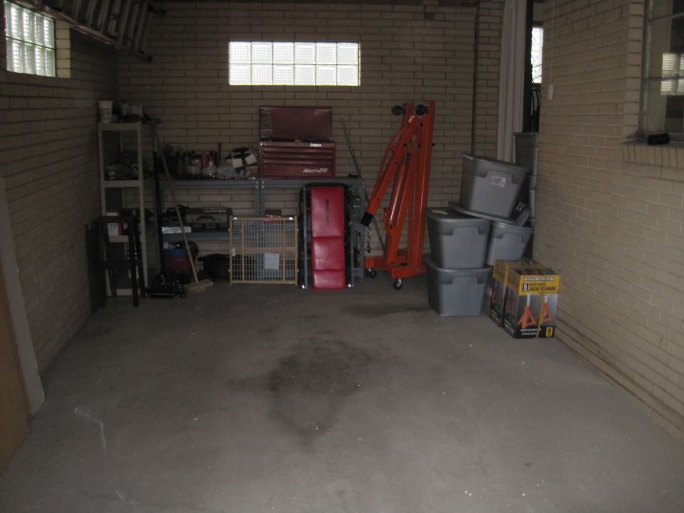 Garage interior with shelves, toolboxes, an engine hoist, storage bins, and a baby gate