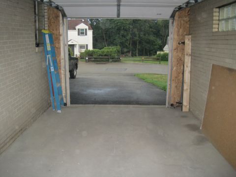 1979 Ford Bronco - A dark-colored truck is partially visible from the side as it sits in a garage, with a house and trees seen through the open door.