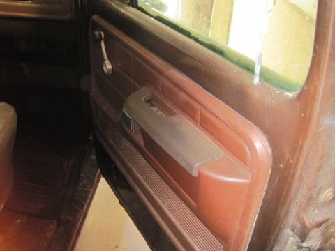 1979 Ford Bronco - Close-up of a brown interior door panel, showing the manual window crank and armrest.