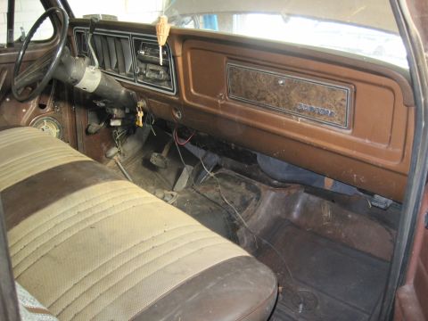 1979 Ford Bronco - The interior of an older vehicle shows a two-tone bench seat and a dashboard with woodgrain trim.