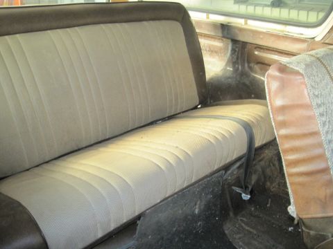 1979 Ford Bronco - The interior of a vehicle shows a rear bench seat with a patterned fabric and brown trim, along with a seatbelt.