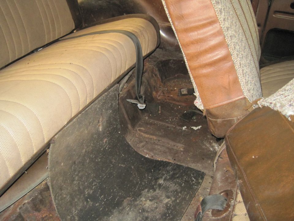 Interior view of a vehicle showing worn seats, floor mats, and seatbelts