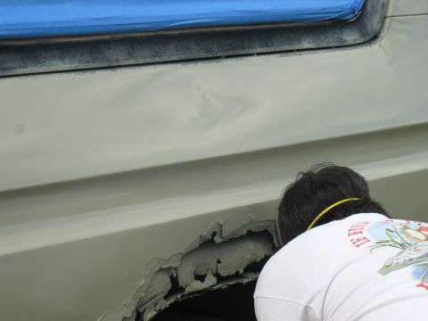 1978 Ford Bronco - Close-up of a person examining significant rust damage on a vehicle's wheel well, with blue masking tape visible on the window frame.