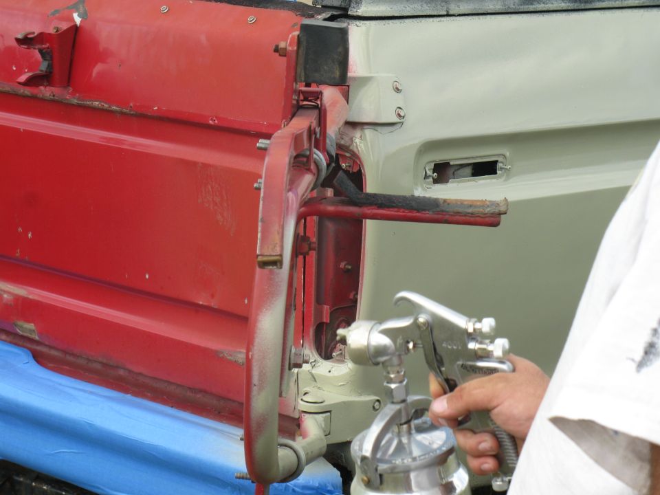 Spray gun painting a car door hinge mechanism. Red and light gray panels visible