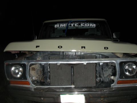1978 Ford Bronco - The front of a Ford truck is shown with the hood up, revealing the engine bay and grille area.