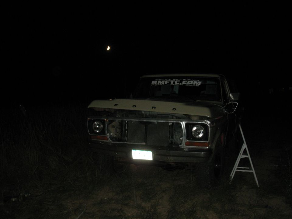 Ford truck with hood open, grille missing, at night