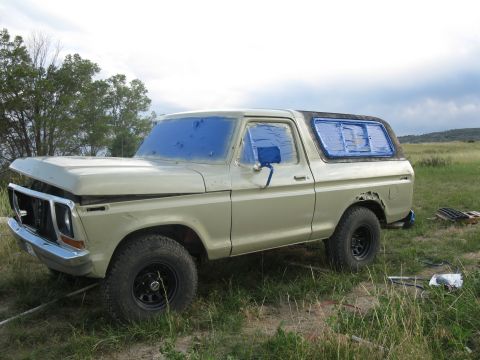1978 Ford Bronco - A 1978 Ford Bronco sits in a field, its windows covered in blue masking tape, suggesting preparation for painting.