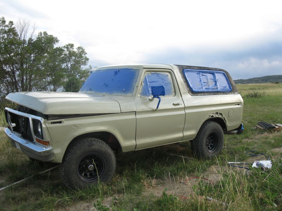 1978 Ford Bronco with blue tape on windows, parked in a grassy field