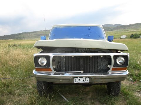 1978 Ford Bronco - A weathered truck sits in a grassy field, its front end exposed with the hood up and grille removed.