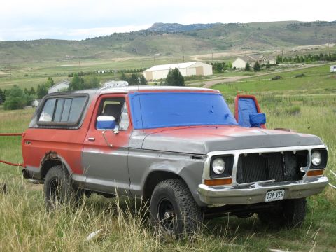 1978 Ford Bronco - This 1978 Ford Bronco, painted in red and grey, is parked in a grassy field with a blue tarp covering the windshield.
