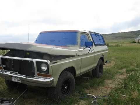 1978 Ford Bronco - A 1978 Ford Bronco sits in a field with its hood up and windows taped, suggesting it is undergoing work.