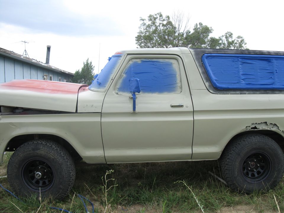 Side view of a 1978 Ford Bronco with blue tape on windows and red-painted hood