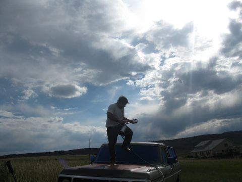 1978 Ford Bronco - A person stands on the hood of a truck, preparing to clean it under a cloudy sky.