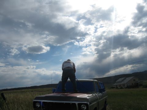1978 Ford Bronco - A person stands on the hood of a 1978 Ford Bronco, silhouetted against a dramatic cloudy sky.