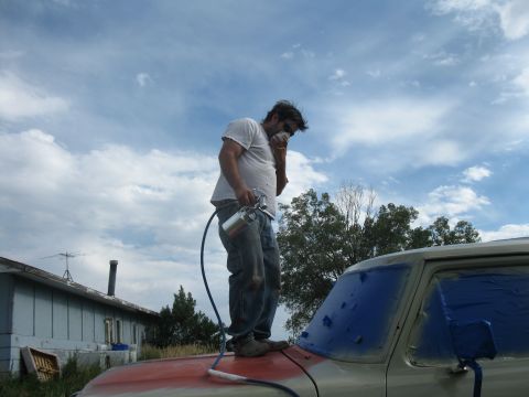 1978 Ford Bronco - A man stands on the hood of a 1978 Ford Bronco, spray painting the vehicle under a cloudy sky.