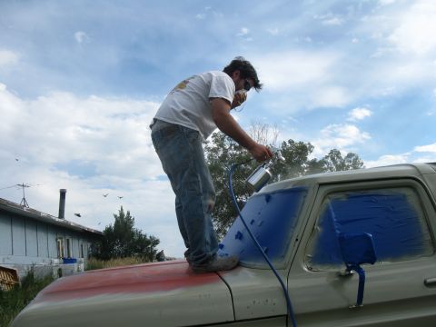 1978 Ford Bronco - Man spray painting a vehicle with windows taped off.