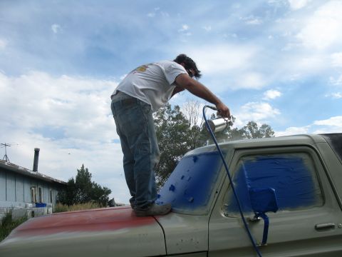 1978 Ford Bronco - A person is spray painting a vehicle that has its windows covered with blue tape.