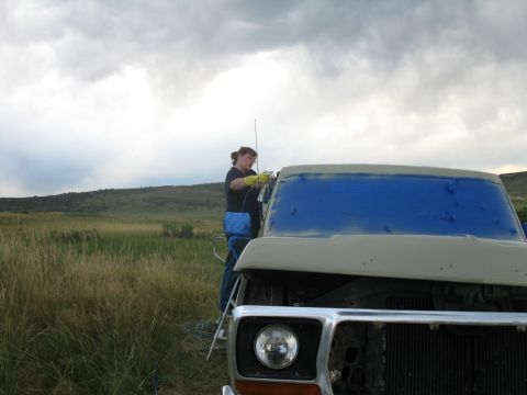 1978 Ford Bronco - A person on a ladder tapes off the windshield of a 1978 Ford Bronco before painting it outdoors.
